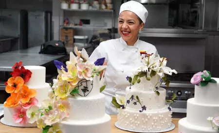 A student smiles behind a row of decorated cakes