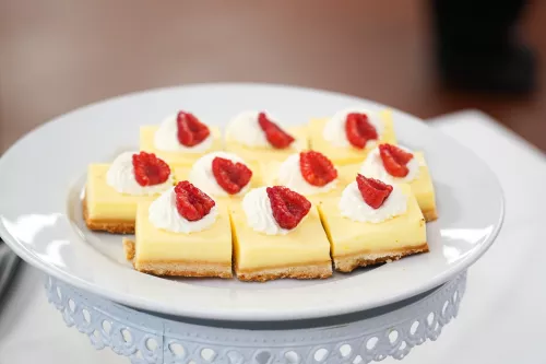 Yellow pastry bars with whipped cream and raspberries on a white plate